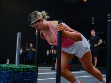 Woman pushing weighted sled during intense workout session.