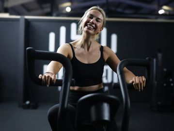 A woman smiling while exercising on a gym machine.