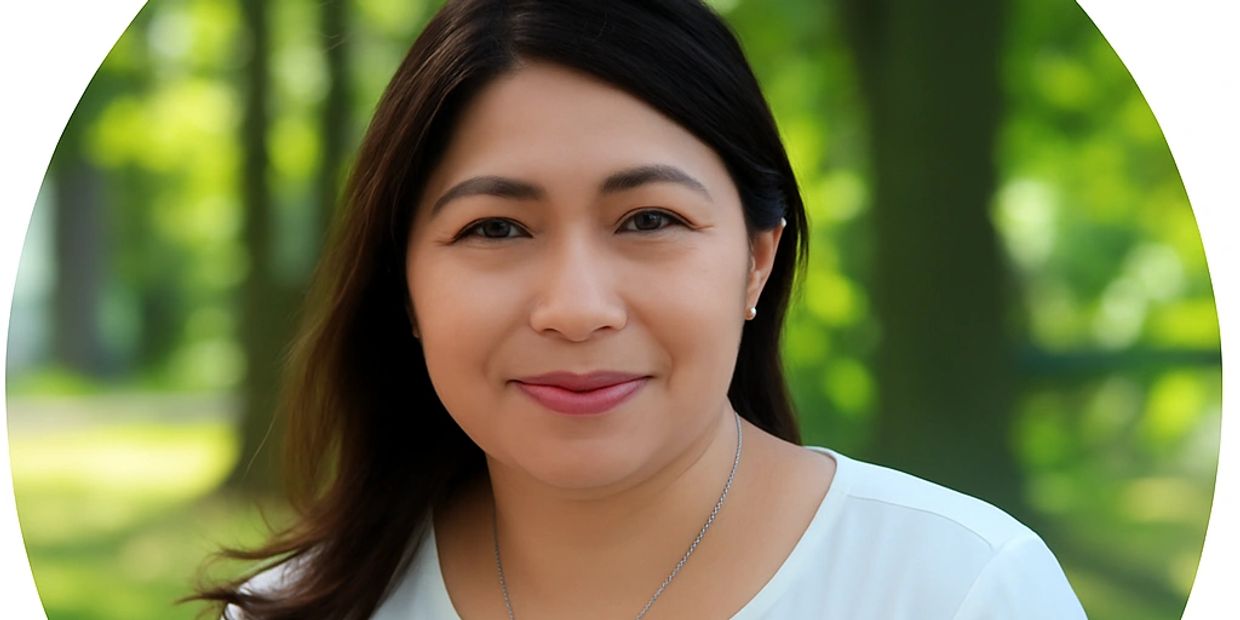 Portrait of a smiling woman in a white top with a natural green background.