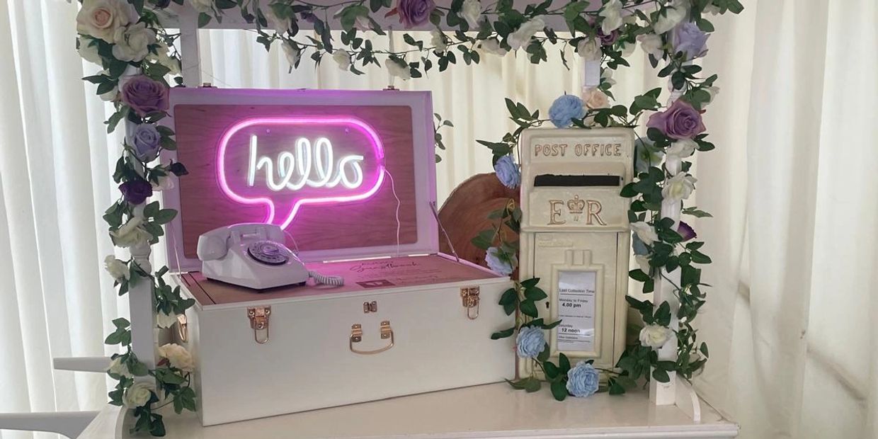 Decorative white cart with flowers, a vintage phone, and a neon 'hello' sign.