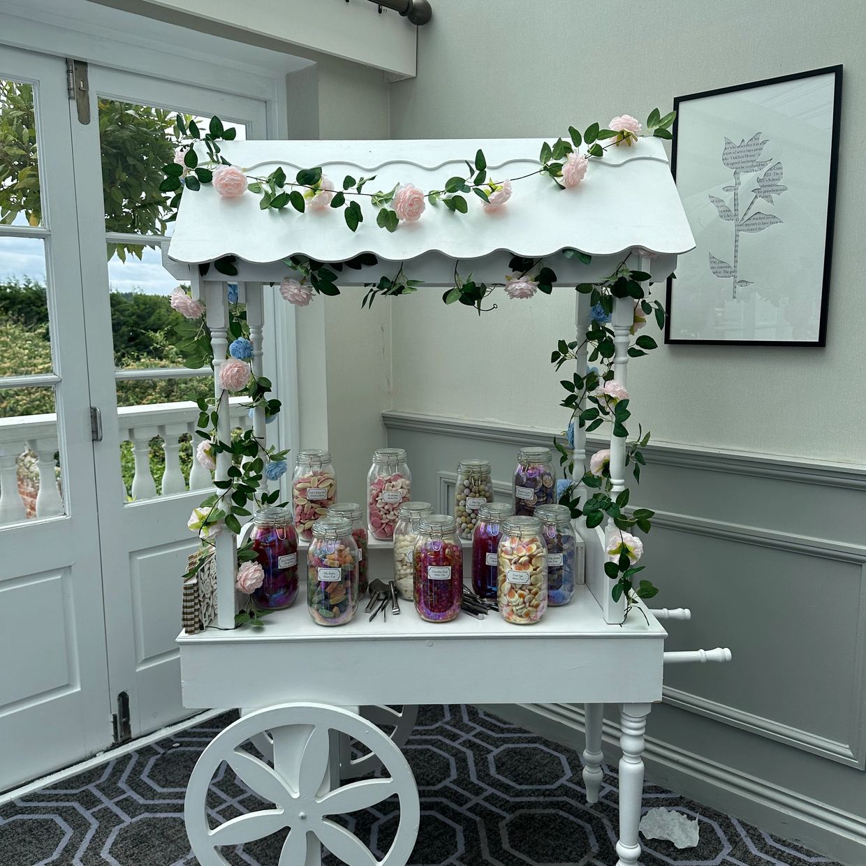 White candy cart decorated with flowers inside a bright room.