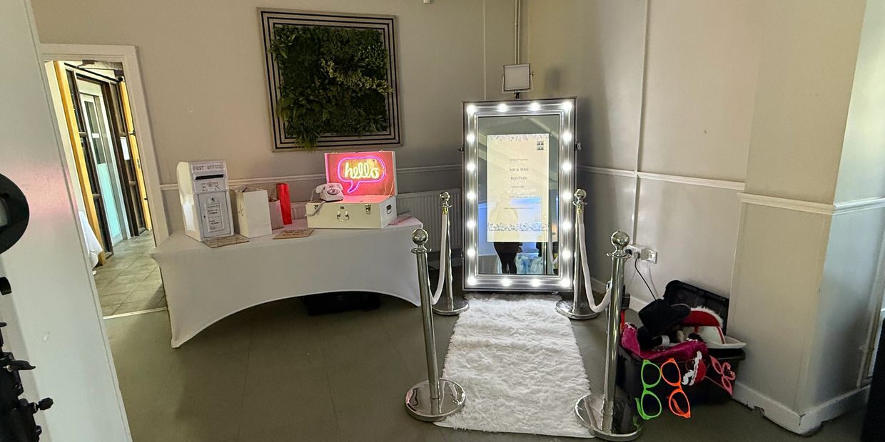 A decorated photo booth setup with a lighted mirror and props in a room.