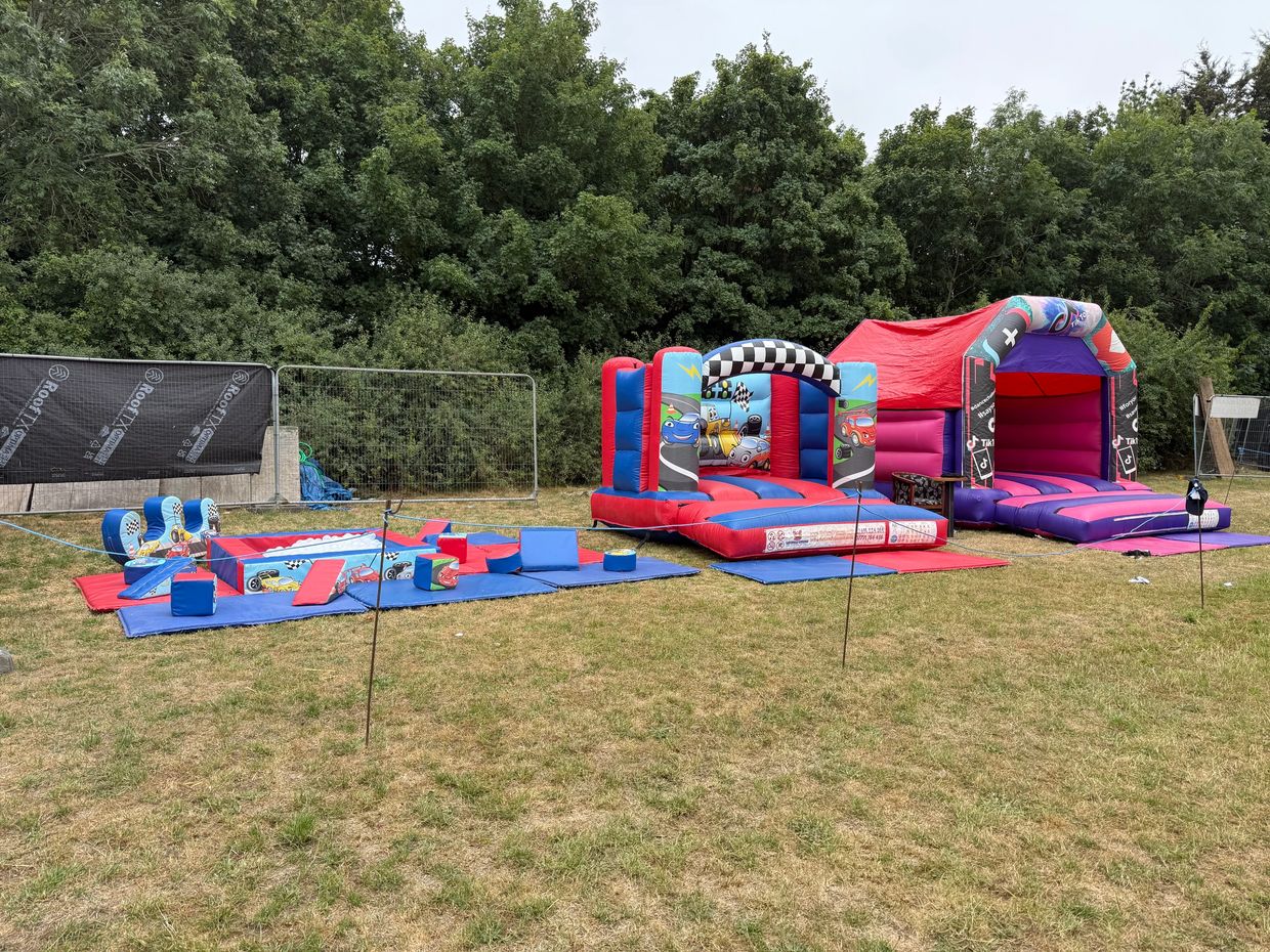 Colorful inflatable play areas on grass with a backdrop of trees.
