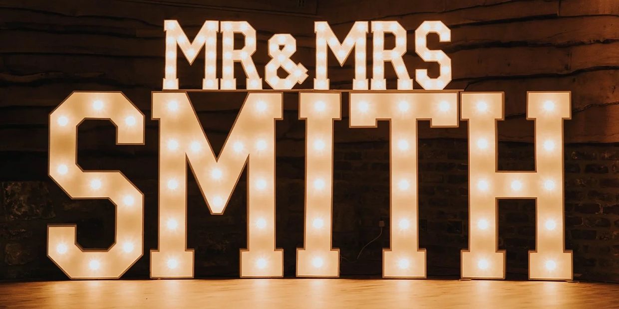 Illuminated marquee letters spelling 'MR & MRS SMITH' on a wooden floor.
