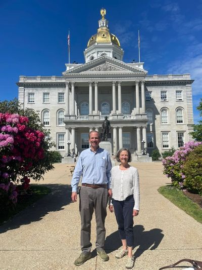 A man and woman stand in front of a grand historic building with a golden dome.