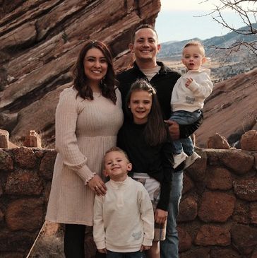 A smiling family of five poses outdoors against a rocky backdrop.