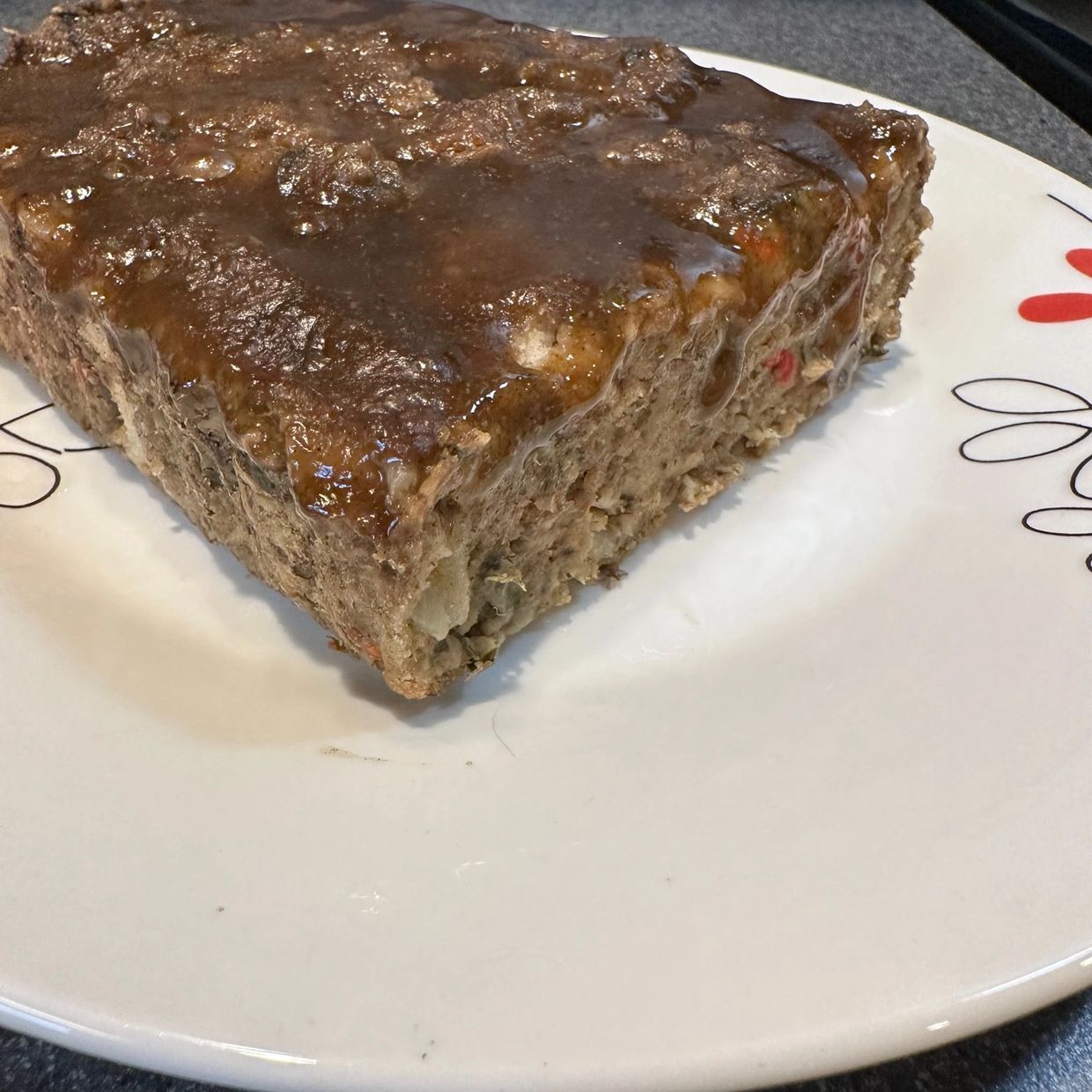 A slice of meatloaf with brown gravy on a plate.