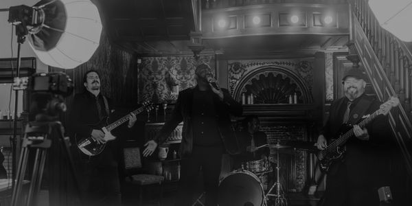 Black and white photo of a band performing with recording lights set up.