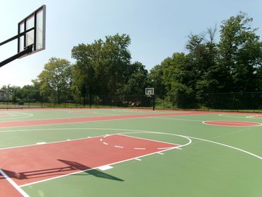 Empty outdoor basketball court surrounded by trees and clear sky.