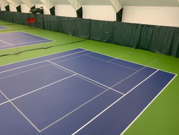Indoor tennis courts with green floors and blue playing surfaces.