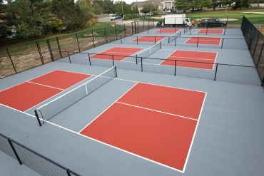 Multiple outdoor pickleball courts with red and gray surfaces.