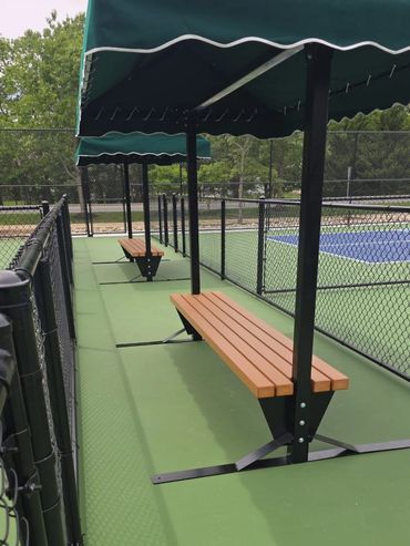 Benches with green canopies next to a fenced tennis court.