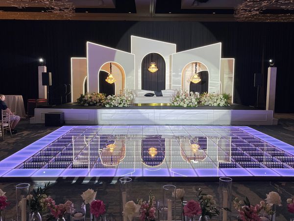 Elegant wedding stage with illuminated dance floor and floral decorations.