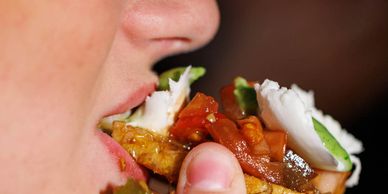 Close-up of a person eating a sandwich with vegetables and cheese.