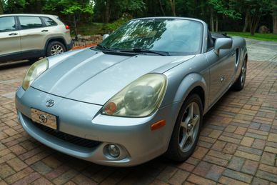 Silver Toyota convertible parked on a brick driveway.