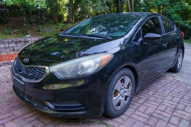 Black Kia sedan parked on a brick driveway.