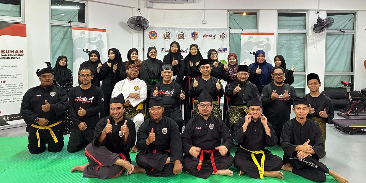 Group of martial artists posing together indoors with thumbs up.