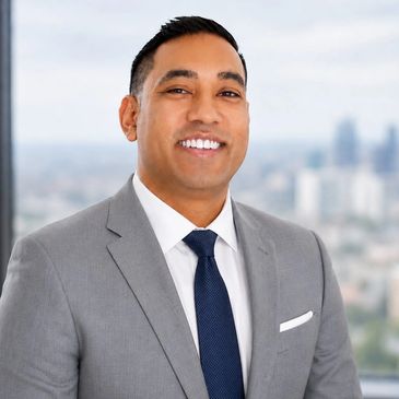 Smiling man in a gray suit and blue tie in an office setting.