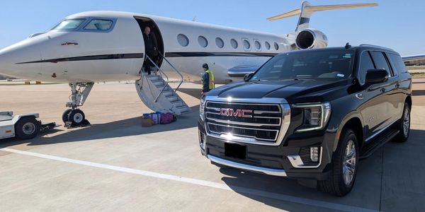 Private jet and black GMC SUV parked on airport tarmac under clear sky.