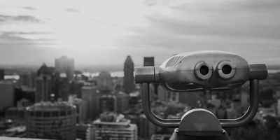 Black and white image of a binocular viewer overlooking a city skyline at sunset.