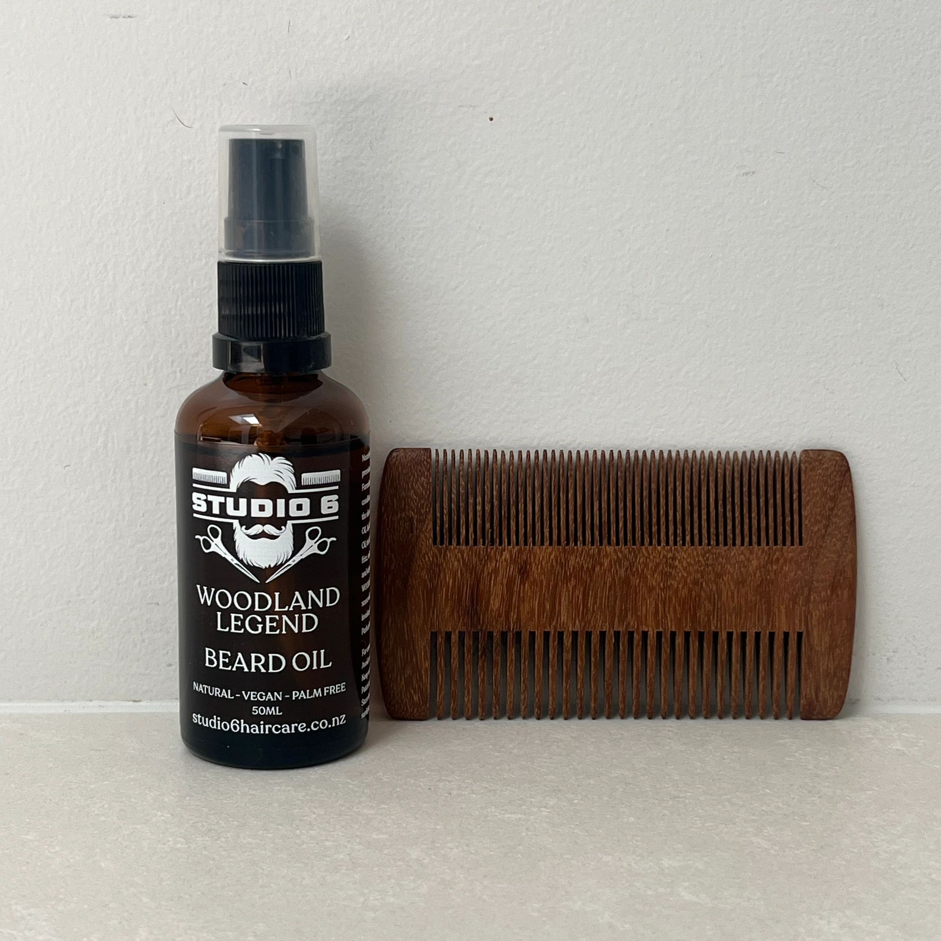 Premium Beard Oil set against a clean white wall with a wooden beard comb displayed next to it.