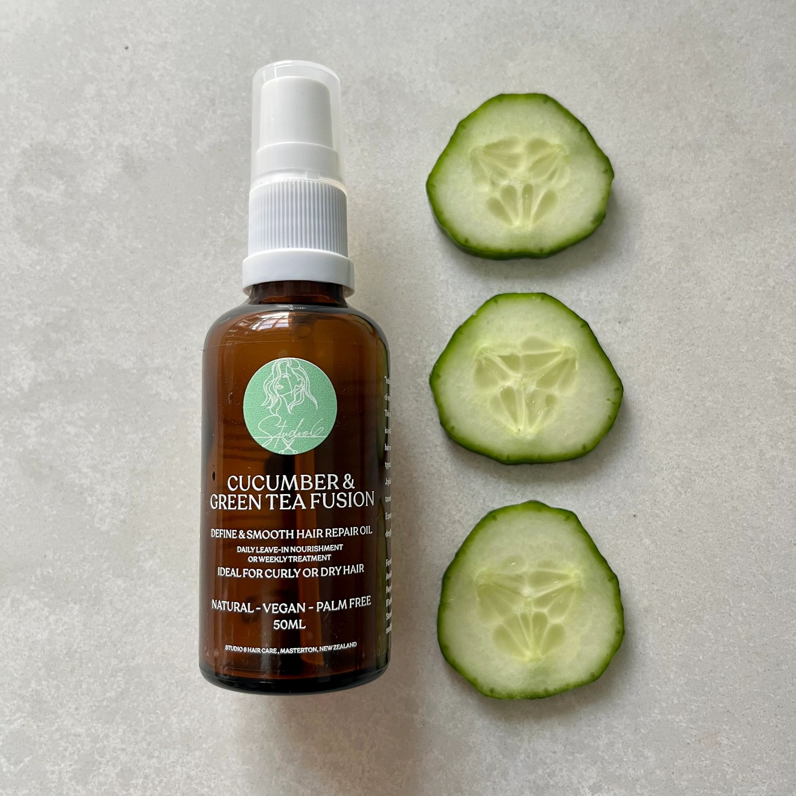 Cucumber & Green Tea scented hair oil product displayed on a clean white stone bench with cucumbers.