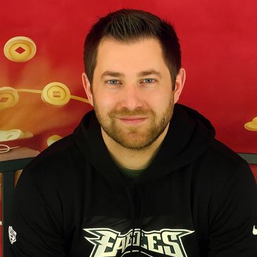 Smiling man wearing a black Eagles hoodie against a red background.