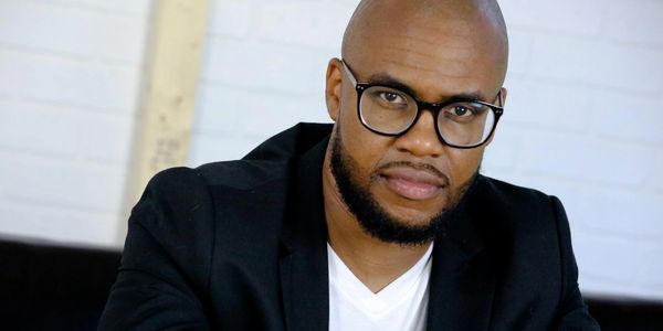 Man with glasses and beard wearing a black blazer and white shirt.