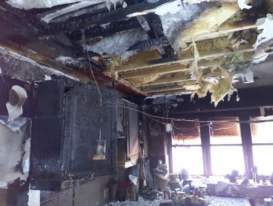 Fire-damaged room with exposed ceiling and charred walls.