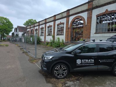 Strata branded vehicle parked in front of a fire damaged building during asbestos demolition survey