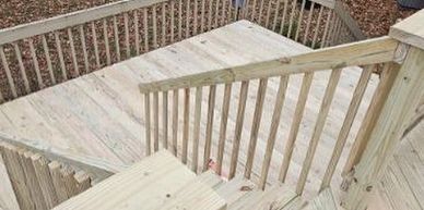 Wooden outdoor stairs and deck with railings in a backyard.