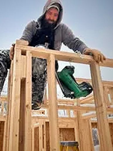 Construction worker building wooden frame with nail gun.