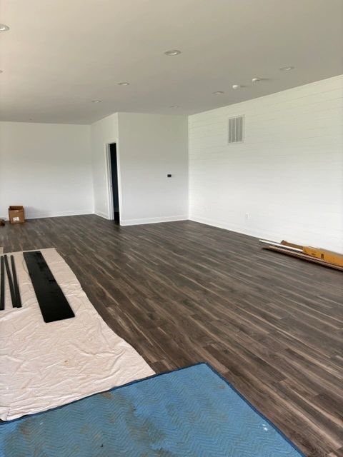 Empty room with dark wood flooring and white walls under renovation.