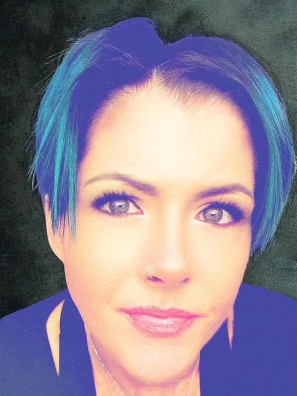 Close-up of a woman with short blue hair and a triangular pendant necklace.