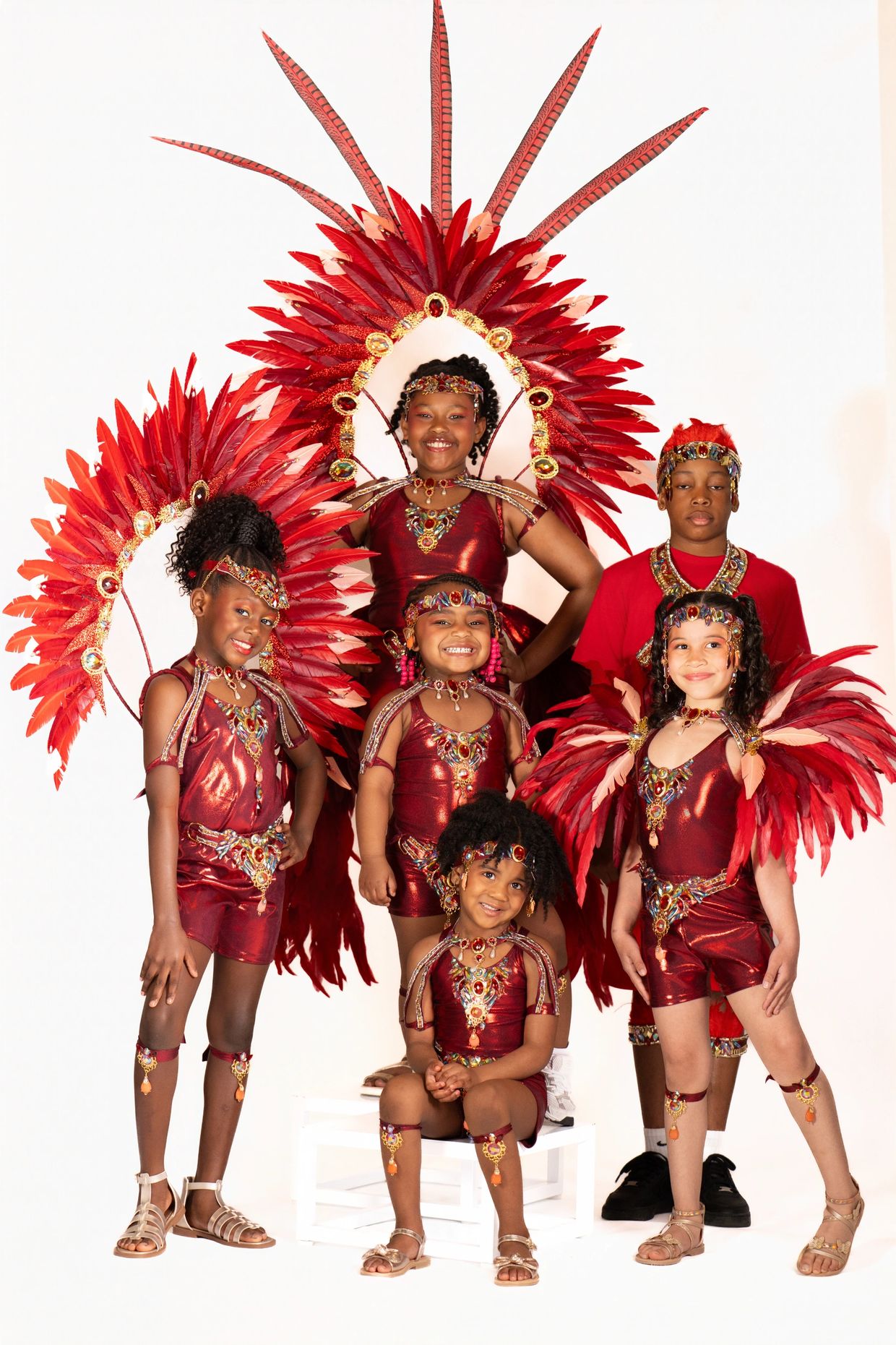 Children dressed in vibrant red carnival costumes with feathered headdresses.