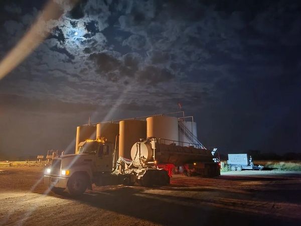 A truck with large tanks under a moonlit, cloudy night sky.