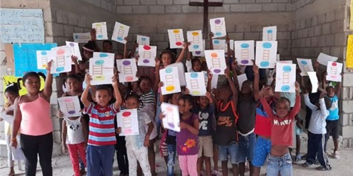 Children proudly holding up their colorful schoolwork in a classroom.