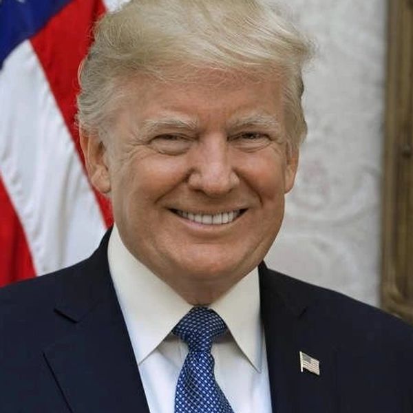 A man in a suit smiling with an American flag in the background.