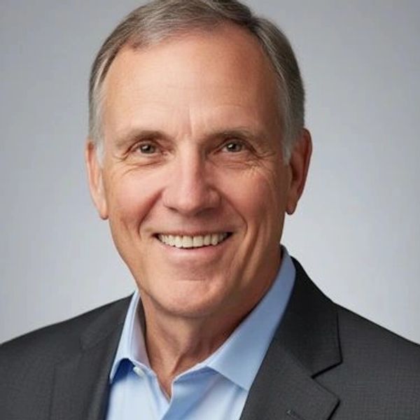 Smiling middle-aged man in a suit jacket and blue shirt against a plain background.