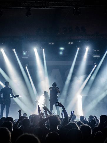 Silhouetted band performing on stage with bright spotlights and cheering crowd.