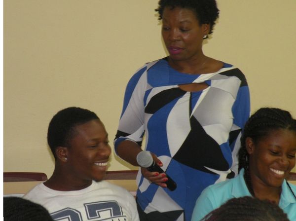 Woman holding microphone talks to smiling young people in a casual setting.