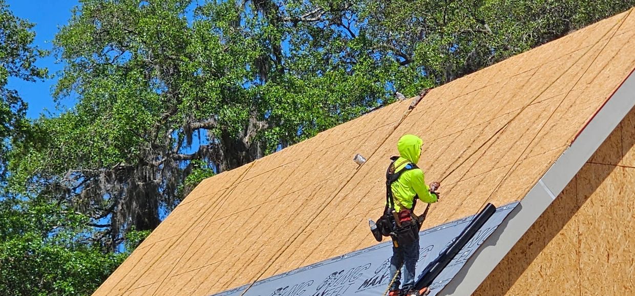 A worker in bright green hoodie installing roofing on a sunny day.
