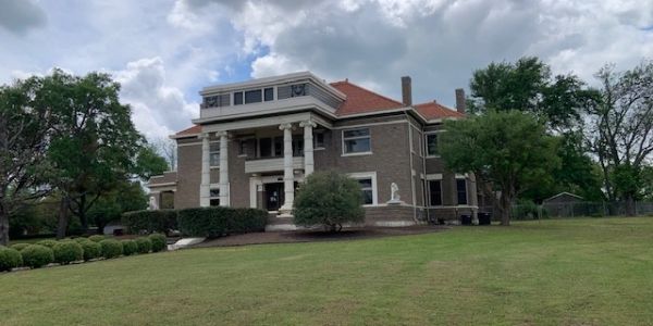 Large historic house with columns and red roof under cloudy sky.
