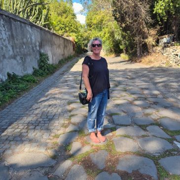 Woman standing barefoot on a cobblestone street.