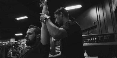 A physical therapist in a gym setting assists a male client with an overhead arm stretch