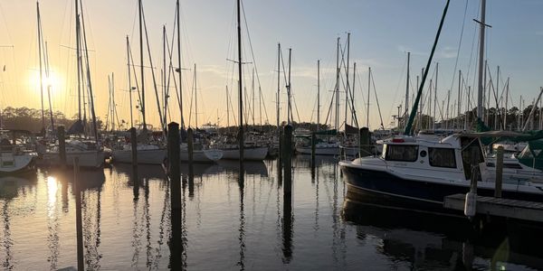 Sunset over a marina with boats and their reflections in calm water.