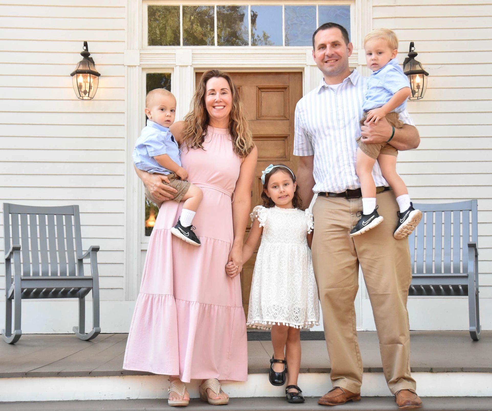 A happy family of five posing on a porch in front of their house.