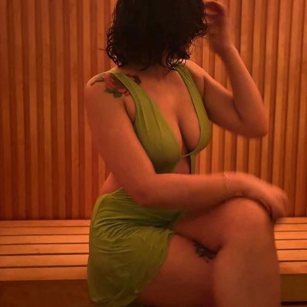 Woman in green dress sitting on wooden bench with tattoos visible.