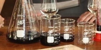 Various glass beakers and a syringe with dark liquid on a wooden table.