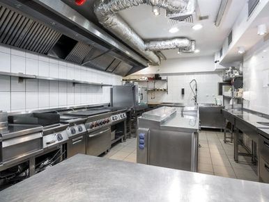 A clean, modern commercial kitchen with stainless steel appliances and white tiled walls.